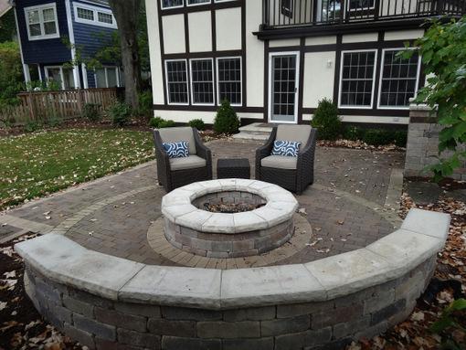 A modular gas valve fire pit incorporated in a clay paver patio.  A curved modular seat wall offers permanent seating. It is an inviting focal point when viewed from inside the house.