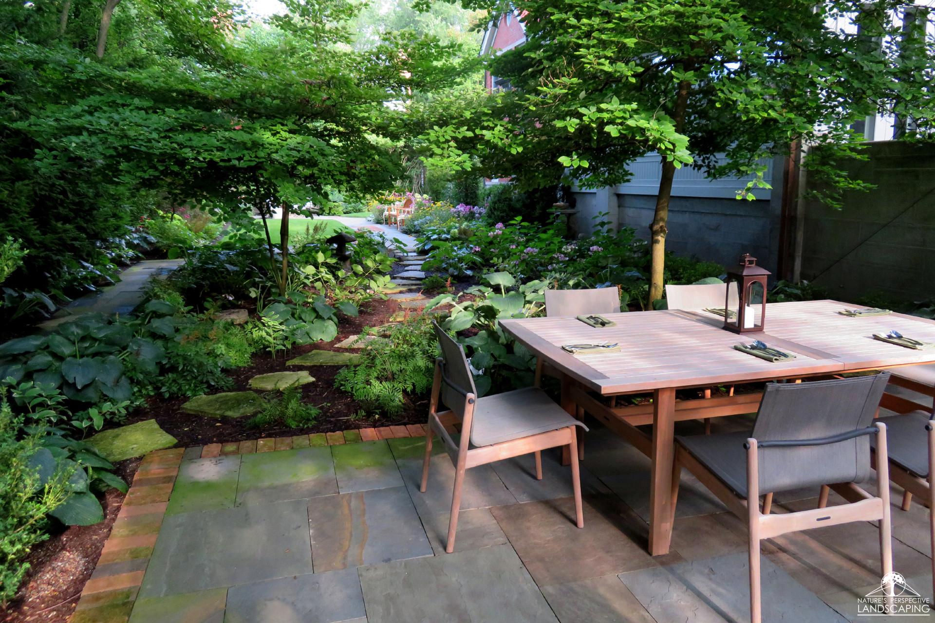 large bluestone and brick patio with modern dining set and shade garden
